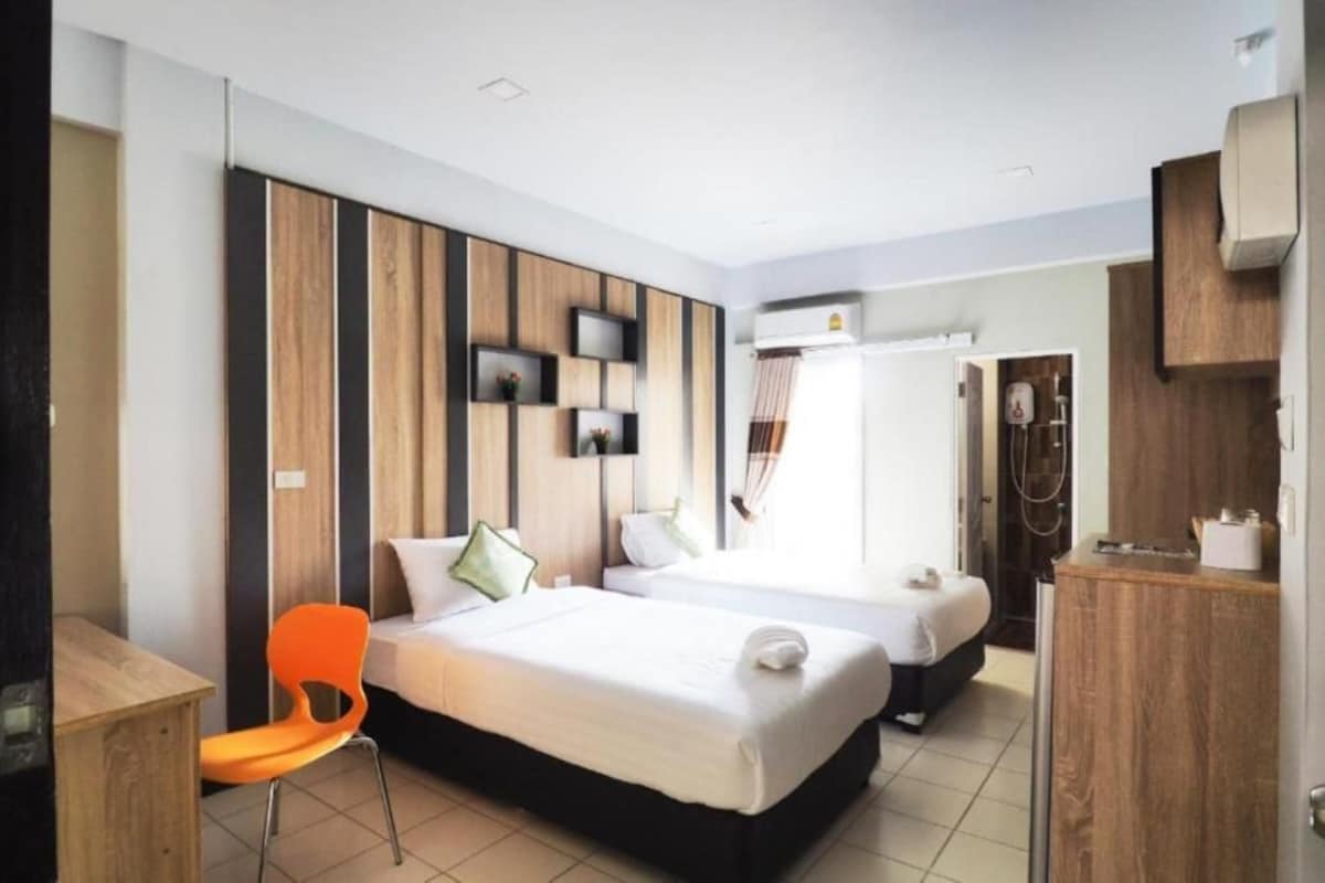 A hotel room with two beds, a desk, a chair, a wardrobe, and a shower area.