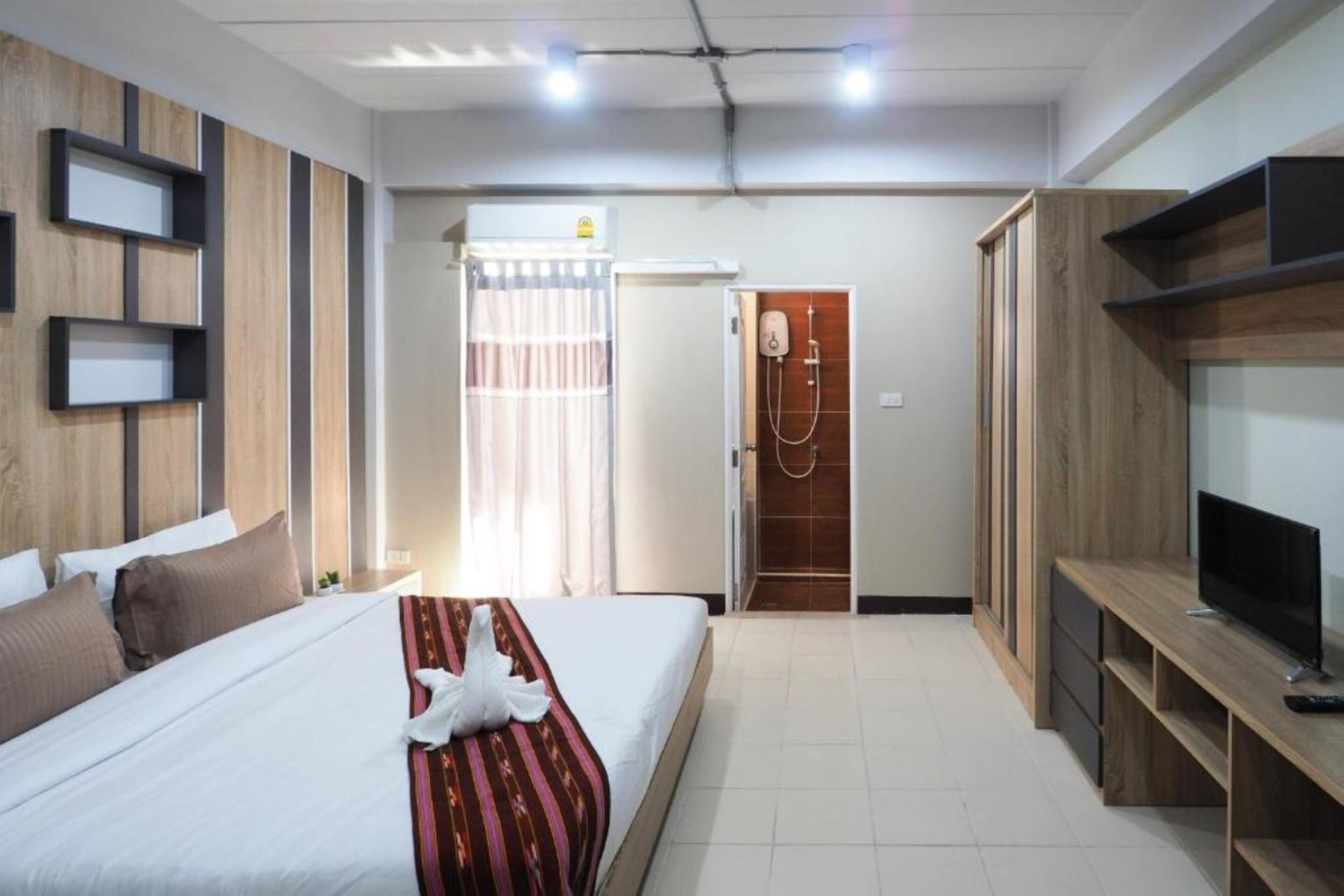 A hotel room with a bed, a TV, a wooden wardrobe, and a shower area.