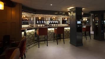Zona de bar con mostrador, varios taburetes y una variedad de botellas y vasos.