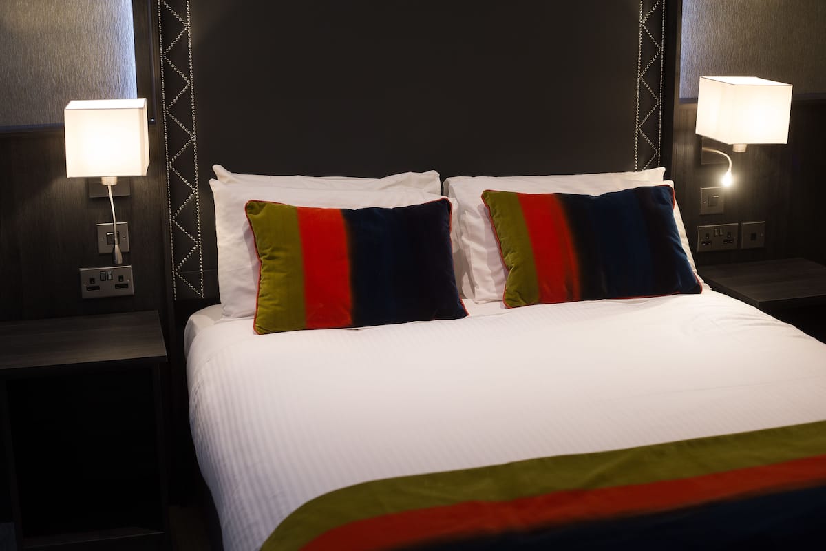 A neatly made bed with white linens and colorful pillows, two bedside lamps, and a dark headboard.