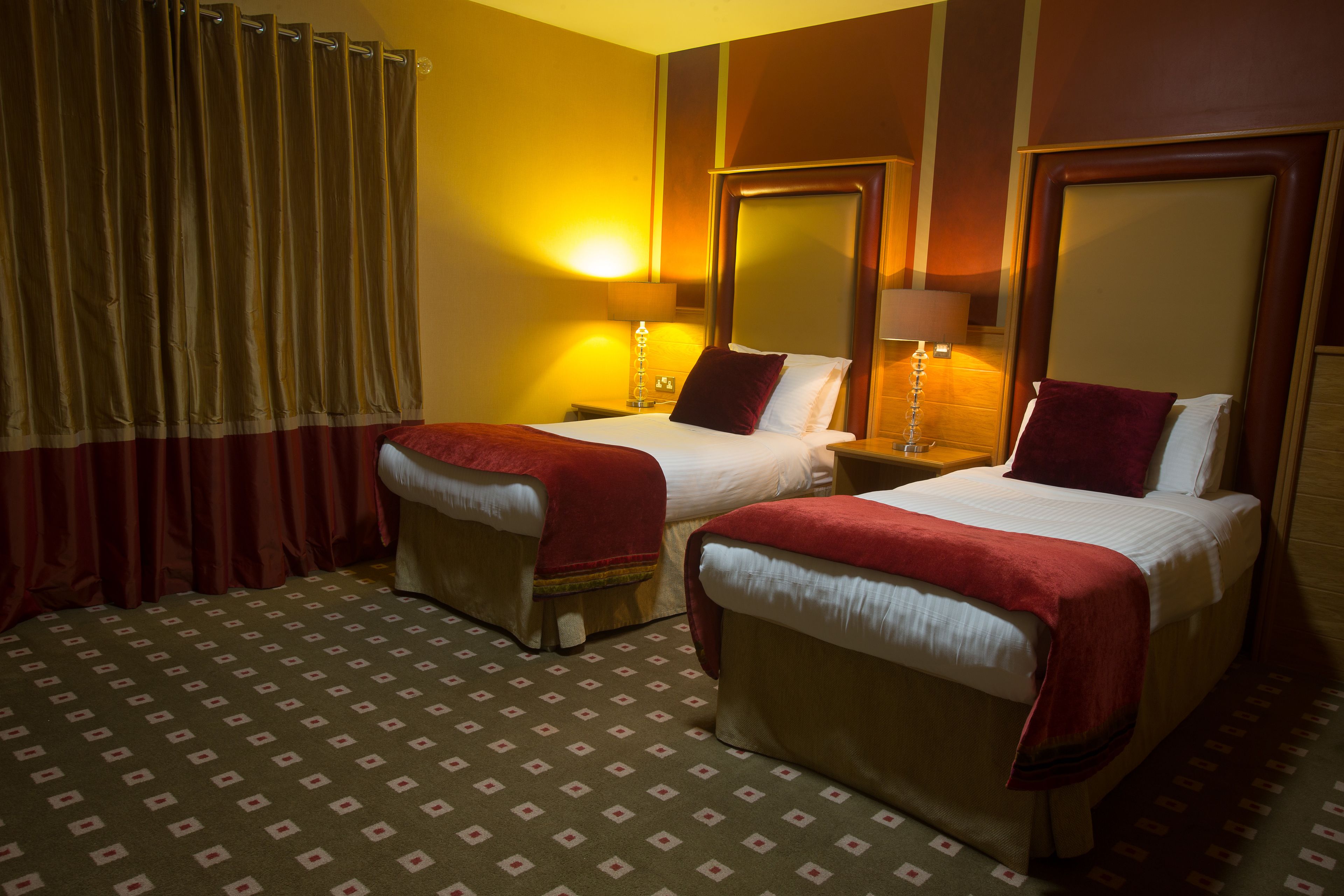 A hotel room with two beds, a large mirror, and a patterned carpet.