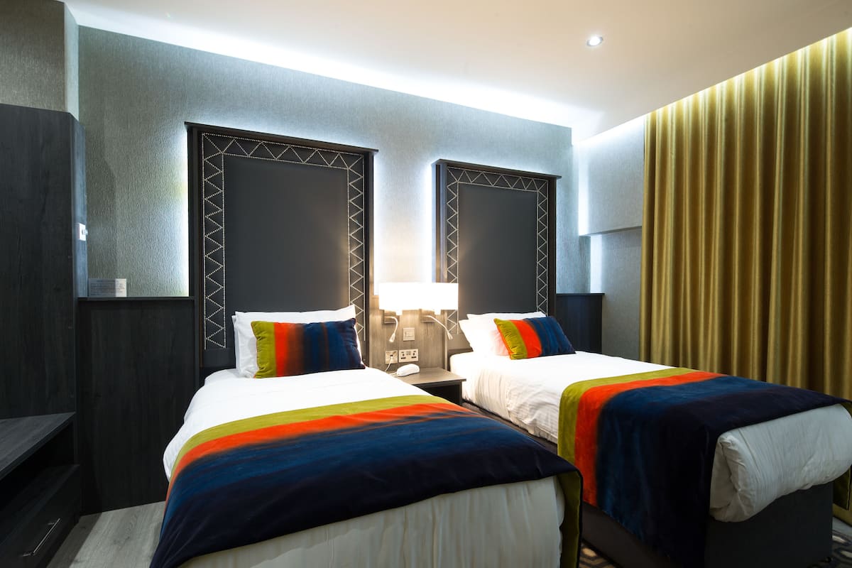 A hotel room with two beds, a desk, and a large window with curtains.