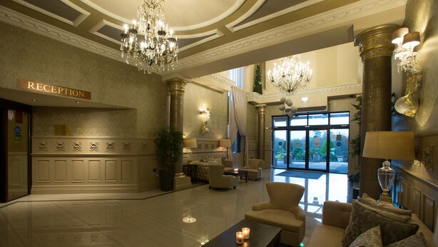 Un vestíbulo amplio con mostrador de recepción, elegantes candelabros, asientos confortables y un gran ventanal con vistas al exterior.