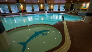Una piscina interior con el logotipo de un delfín, rodeada de ventanas y sillas de descanso.