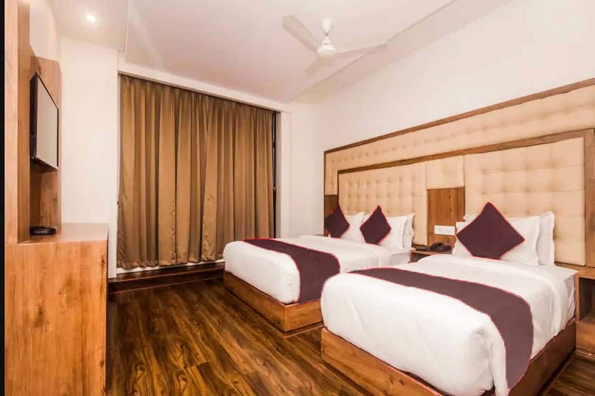 Habitación de hotel con dos camas, suelo de madera, ventilador de techo y un amplio ventanal con cortinas.