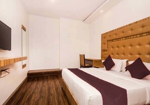 A hotel room with a large bed, a wooden headboard, a flat-screen TV mounted on the wall, and a desk with a chair. - BKC Grand (Mumbai)