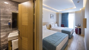Habitación de hotel con puerta de madera, baño con lavamanos y dos camas con ropa de cama azul.