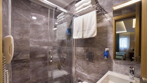 A modern bathroom with a glass-enclosed shower, a white sink, and a mirror reflecting a bedroom.