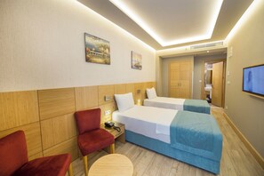 Habitación de hotel con dos camas, un sillón rojo, una mesa redonda pequeña y un televisor montado en la pared.
