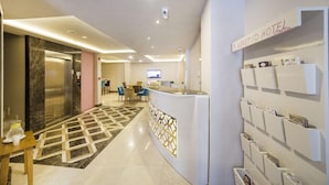 A hotel reception area with a reception desk, a digital screen, a wall-mounted information board, and a check-in counter.