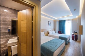 A hotel room with a wooden door, a bathroom with a marble floor, two beds with blue bedding, a small table with a kettle, and a painting on the wall. - The Meretto Hotel Laleli (Istanbul)