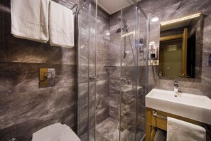 A modern bathroom with a glass-enclosed shower, a white sink, and marble walls.