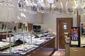 Zona de bufé con diversas opciones de comida, una puerta para personal y un dispensador de bebidas.