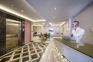 A hotel reception area with a reception desk, a digital screen, a seating area with chairs, and an elevator. - The Meretto Hotel Laleli (Istanbul)