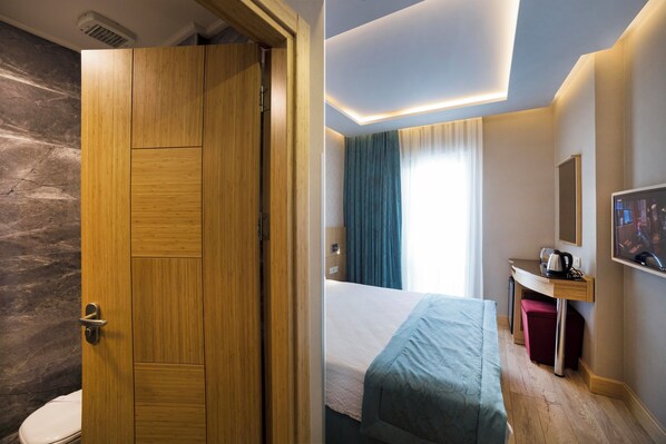 A hotel room with a wooden door, a bed, a desk, a mirror, and a television.