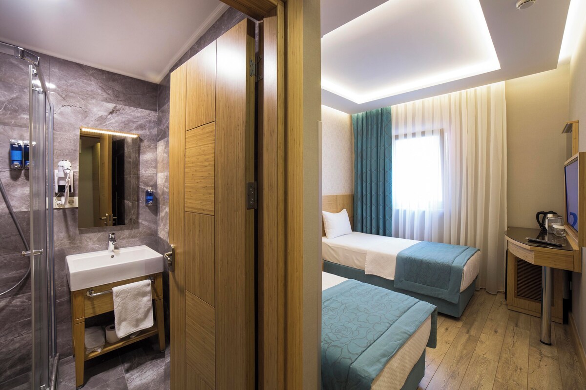 A hotel room with a bathroom, a bed, a desk, and a TV.