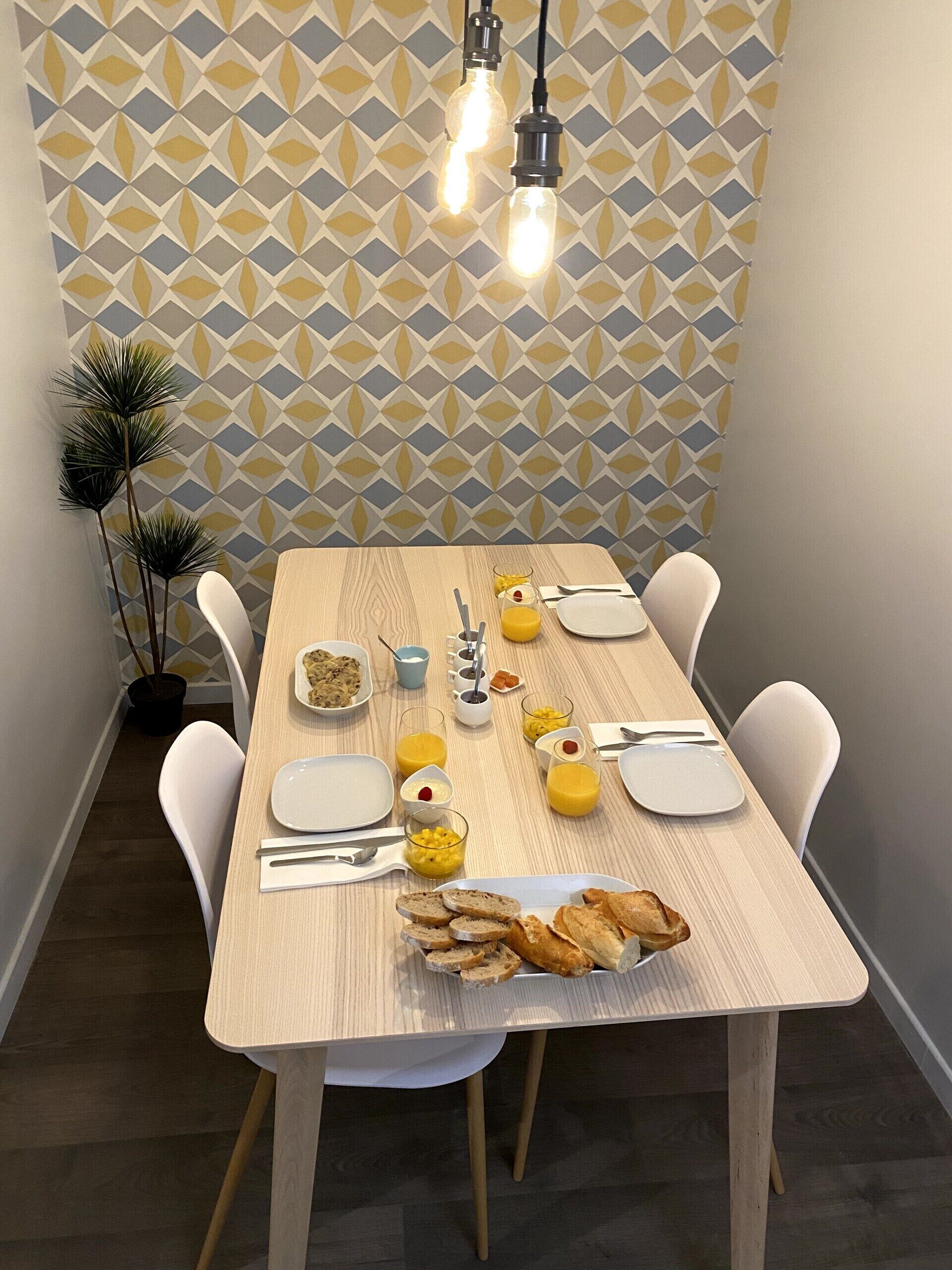 A dining table set with plates, cutlery, and food items, with a geometric patterned wall in the background.