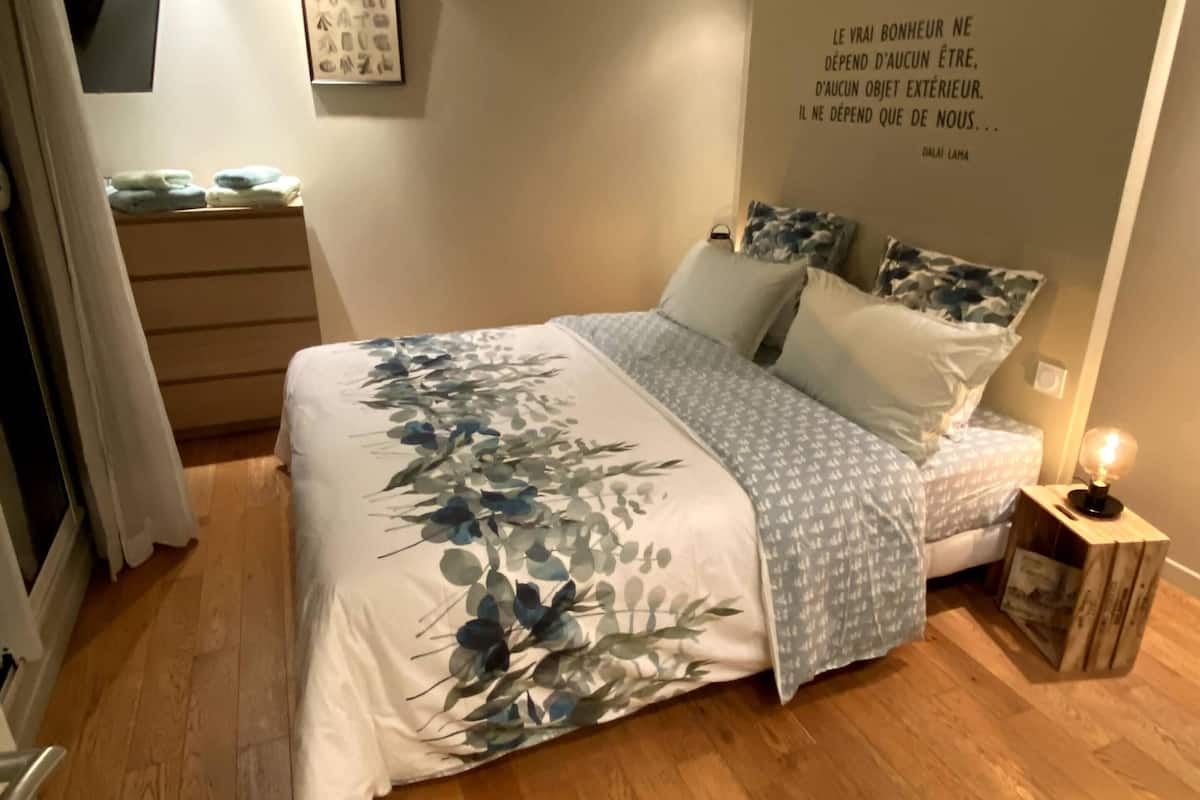 A bedroom with a bed, a dresser, a bedside table with a lamp, and a wall quote.