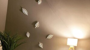 Ein Badezimmer mit braunen Wänden, einem Topf mit Pflanze, zwei Stapeln Handtücher, einer Lampe und Wandbildern mit Blättern.