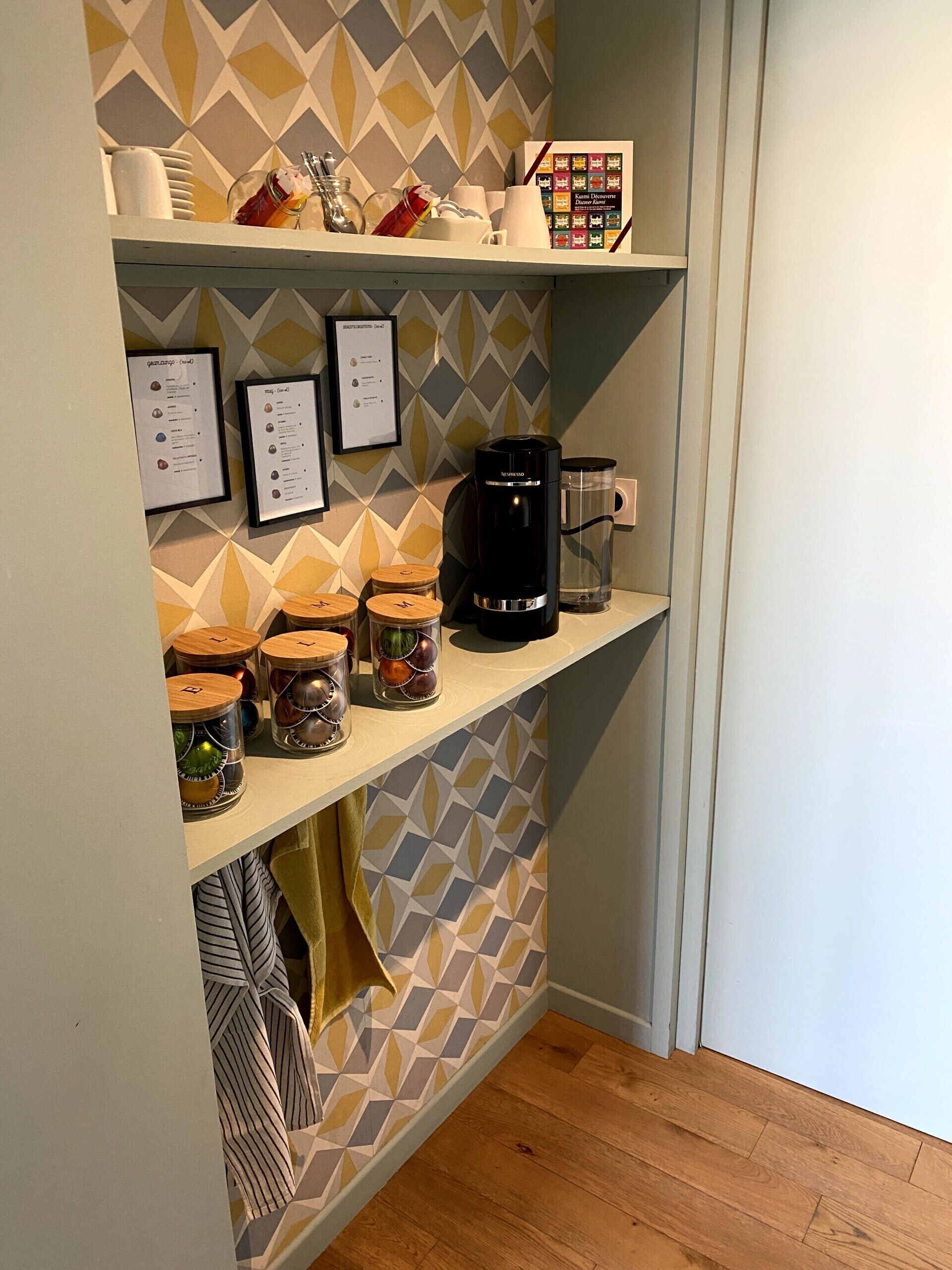 A kitchen with a geometric patterned backsplash, a coffee maker, jars with lids, and a menu board.