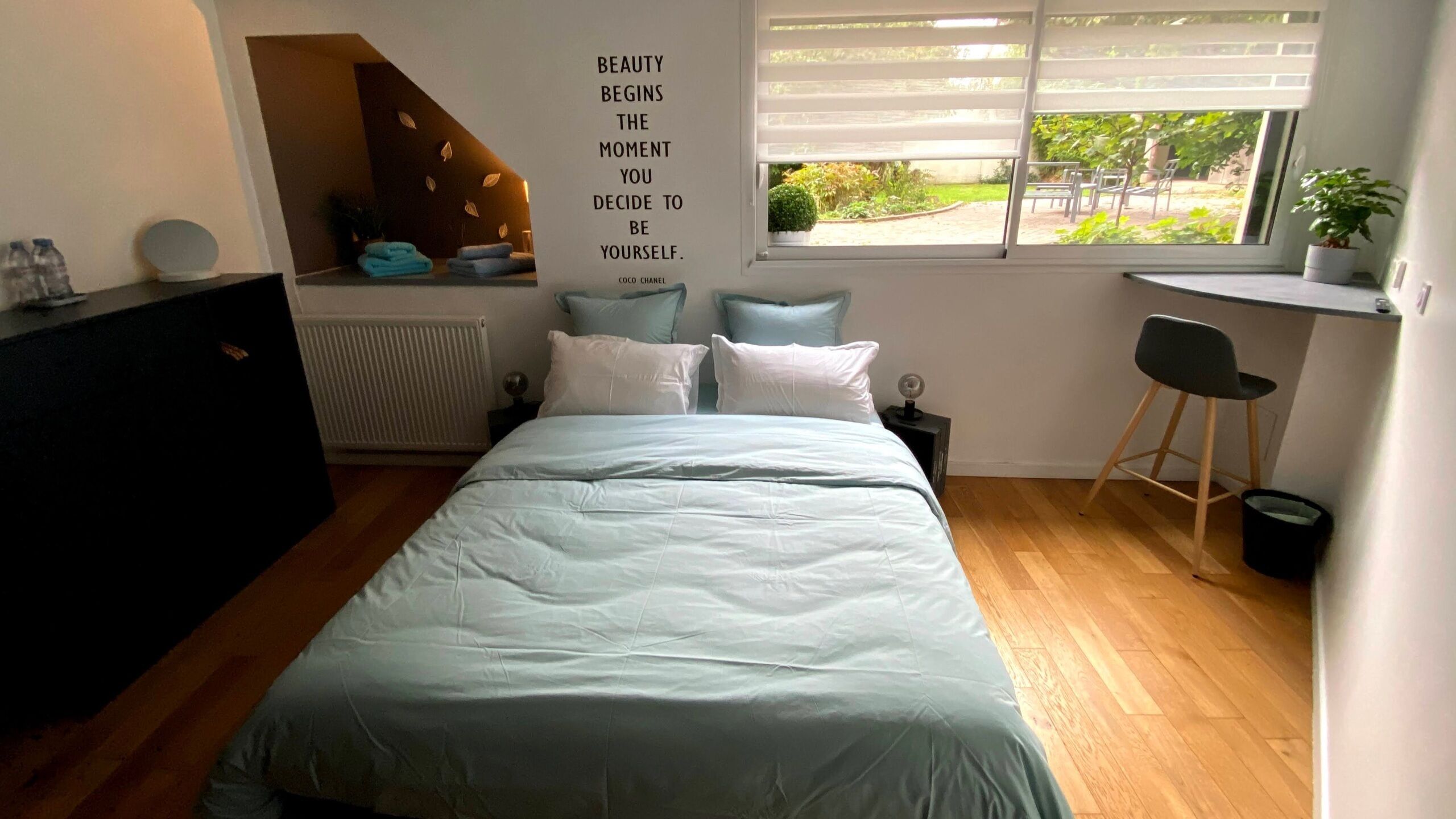 Et soveværelse med seng, skrivebord, stol, radiator og et vindue med udsigt til grønne områder.