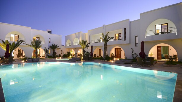 A swimming pool with lounge chairs and umbrellas, surrounded by white buildings with arched windows and balconies. - Palm Djerba Suites (Mezraia)