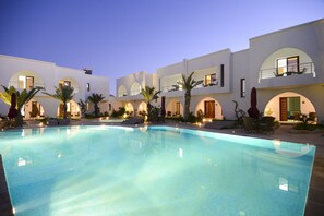 A swimming pool with lounge chairs and umbrellas, surrounded by white buildings with arched windows and balconies. - Palm Djerba Suites (Mezraia)