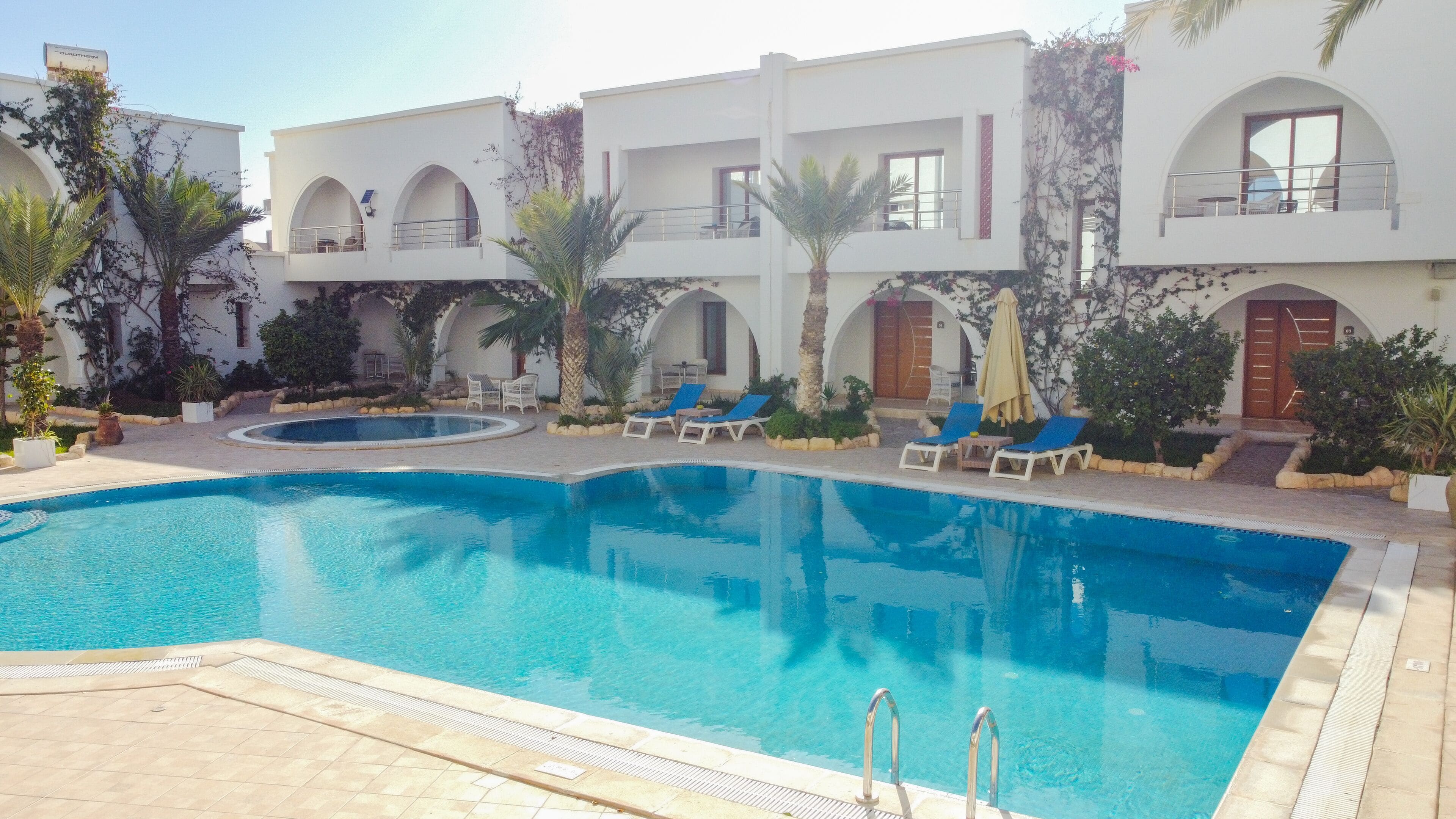 A swimming pool with lounge chairs and a building with arched windows and balconies.