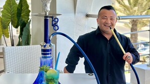 A person holding a hookah with a blue hose, a glass with a blue drink, and a decorative hookah base. - Palm Djerba Suites (Mezraia)
