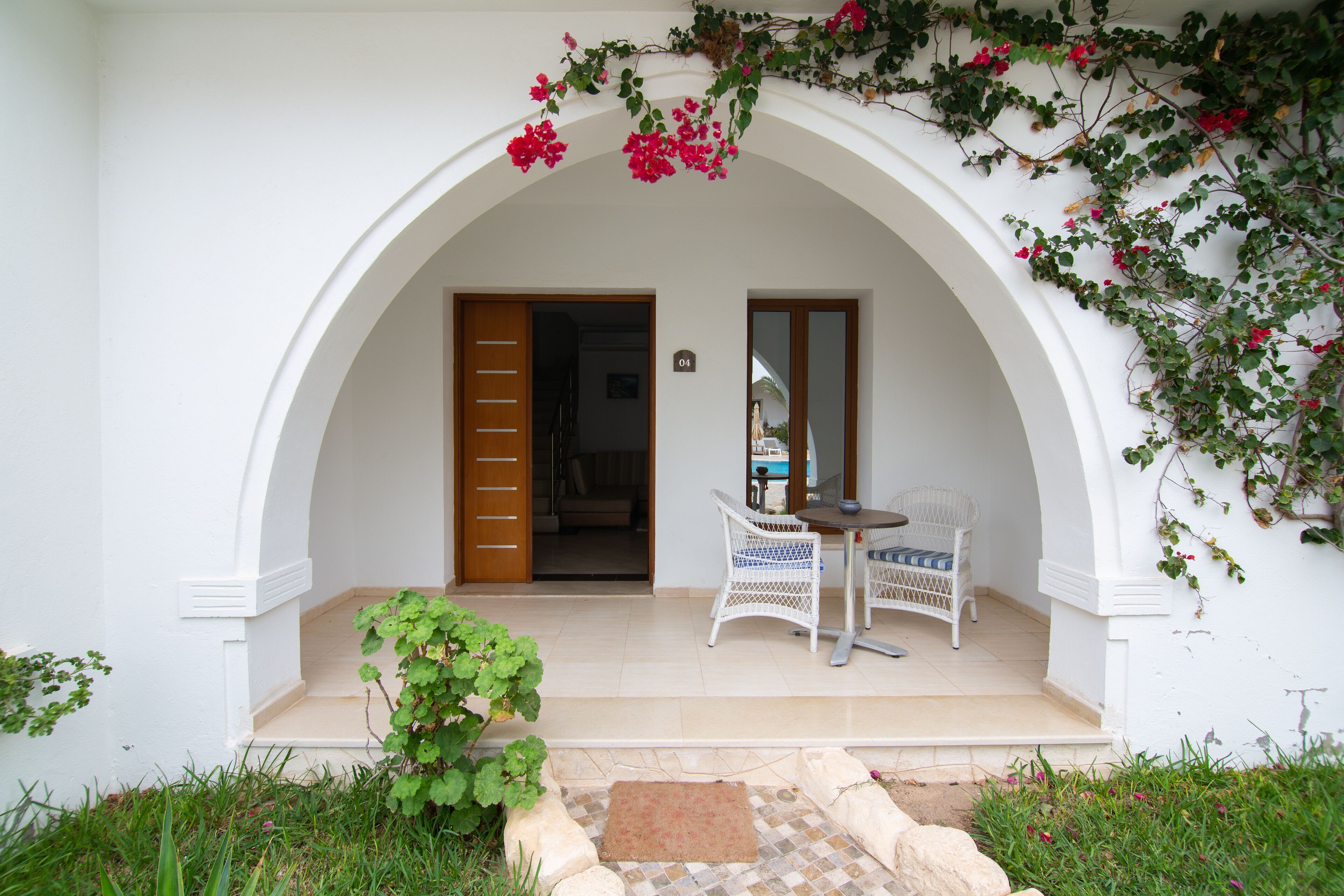 A white building with an arched entrance, a small table with chairs, and a door leading inside.