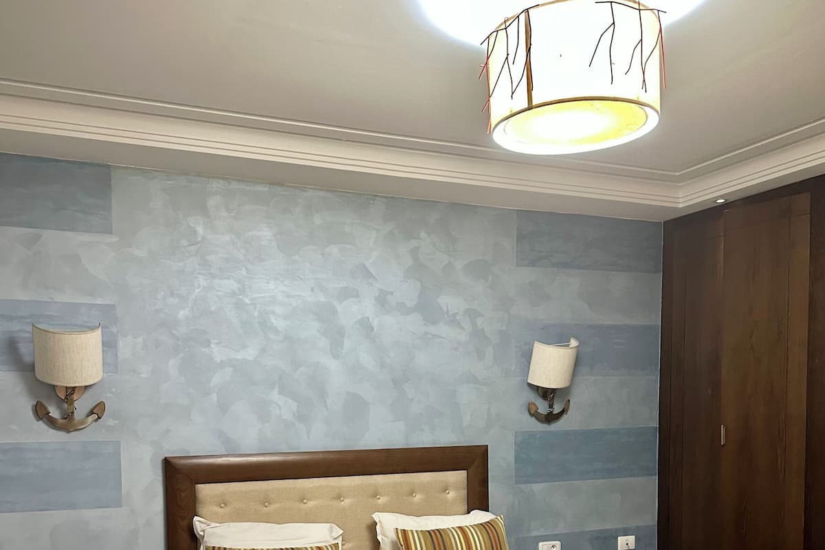 A bedroom with a large bed, two bedside tables, a nightstand, a floor lamp, and a wardrobe.