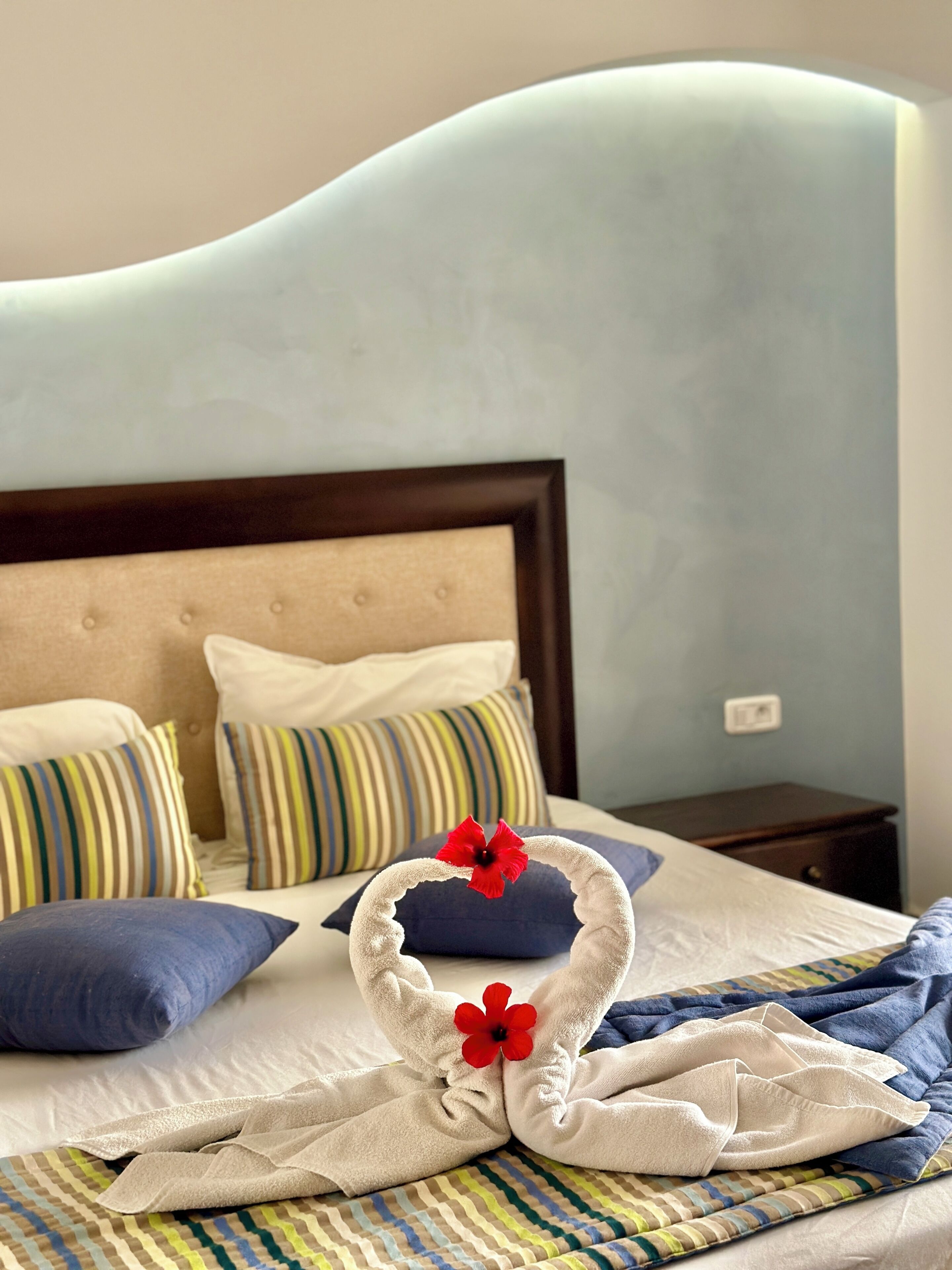 Un lit bien fait, agrémenté d’oreillers à rayures, d’un oreiller bleu et d’une serviette décorative ornée de fleurs rouges.