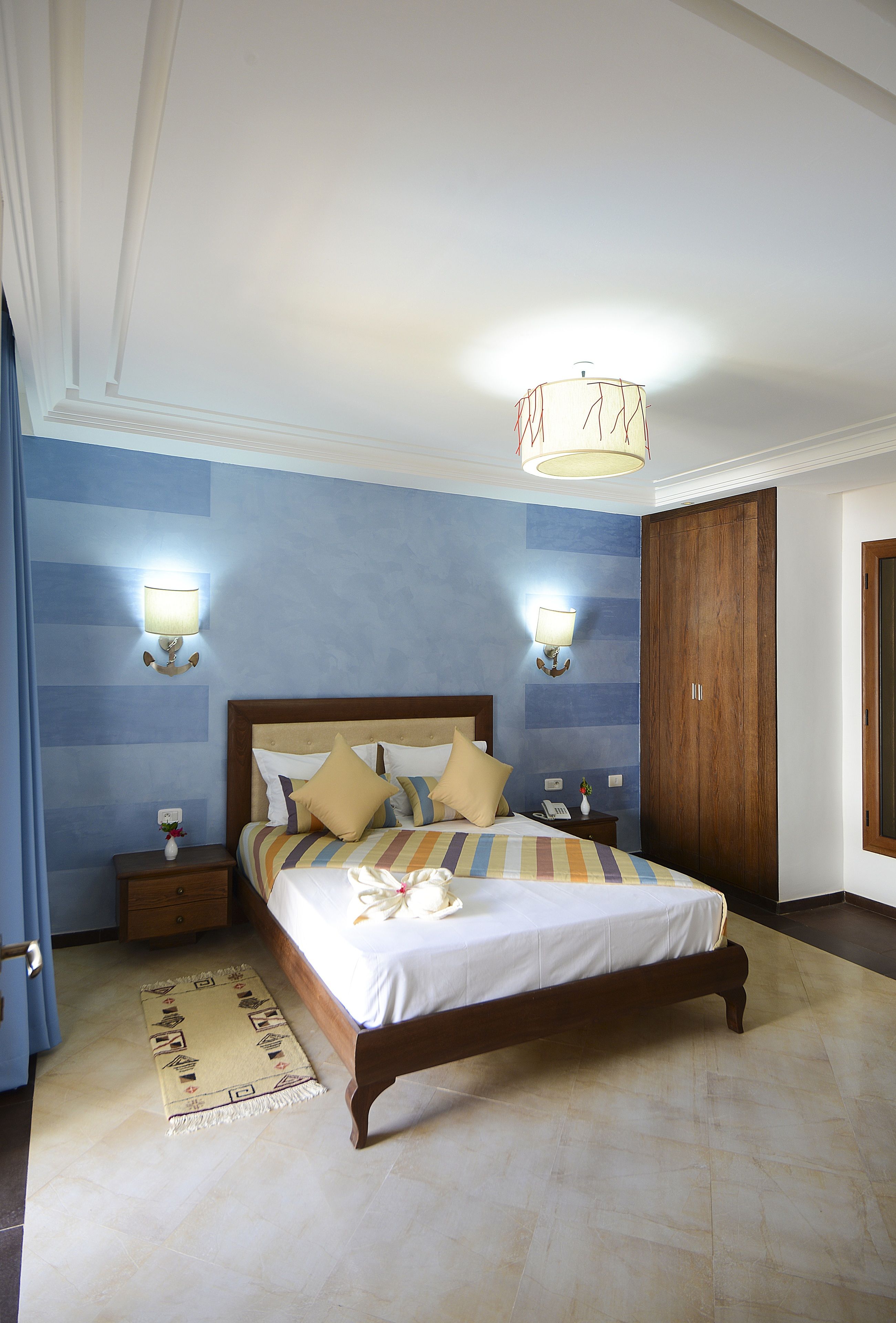 A bedroom with a wooden bed, two bedside tables, a nightstand, a wall-mounted lamp, and a wardrobe.