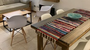 A modern living room with a sofa, a dining table with chairs, a coffee table, and a small shelf with a lamp.