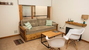 A compact living space with a sofa, two chairs, a small table, a window, and a shelf with items.