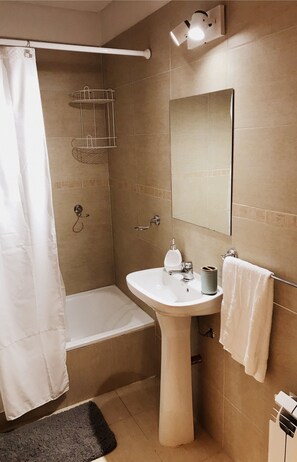 A bathroom with a pedestal sink, a bathtub, a shower curtain, a towel rack, and a mirror.