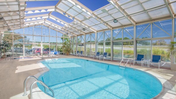 A covered swimming pool with clear glass walls, surrounded by lounge chairs and a view of the outdoors. - Baymont Inn and Suites (Corbin)