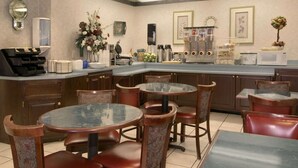 A modern kitchen with a central island, bar stools, and a dining area with round tables and chairs. - Baymont Inn and Suites (Corbin)