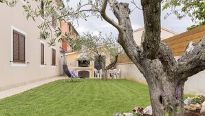 Ein gepflegter Garten mit Rasenfläche, einem Baum und einer Terrasse mit Gartenmöbeln.