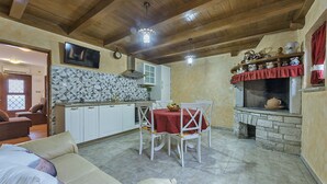 Ein gemütlicher Wohnbereich mit Esstisch, weißen Stühlen, einer Couch und einer Küche mit weißen Schränken und einer gefliesten Rückwand.
