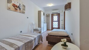 Ein Schlafzimmer mit zwei Betten, einem kleinen Tisch mit einer Vase, einem Bild an der Wand und einer Tür zu einem Badezimmer.
