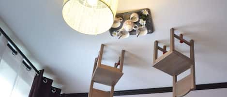 Una habitación con una silla colgante de madera, un estante de pared con tazas y platos, y un estante de madera con bloques.