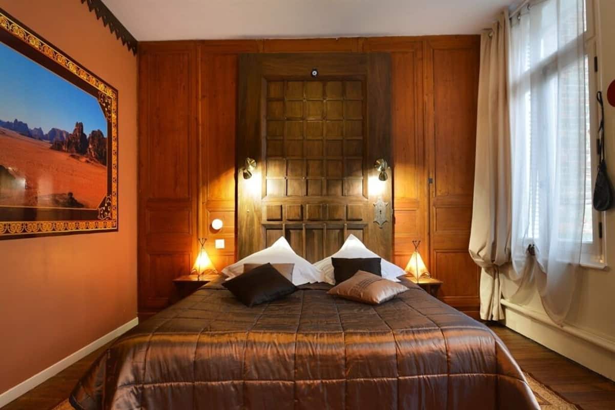 Un dormitorio con una cama grande, paneles de madera en las paredes, un ventanal con cortinas y un cuadro enmarcado.