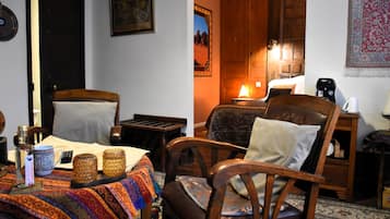 A cozy room with a bed, two wooden chairs, a table with a colorful tablecloth, a lamp, and a wall-mounted picture.