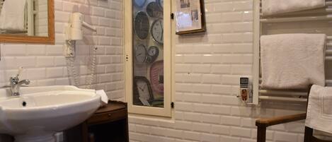 A bathroom with a white sink, mirror, and wooden chair. There are multiple clocks on the wall and a framed picture.