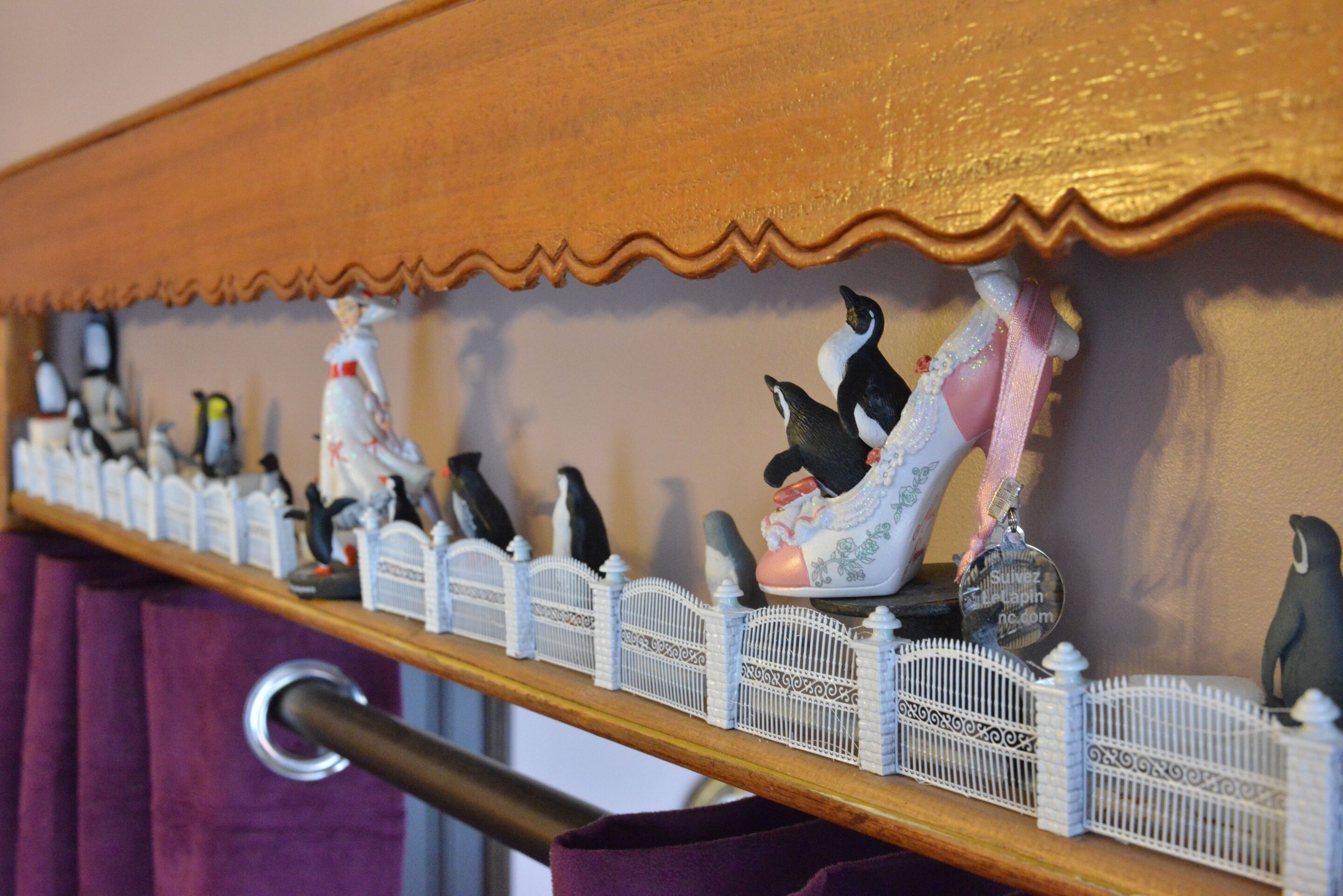 Een plank met decoratieve pinguïnbeeldjes en een witte, hekachtige constructie.