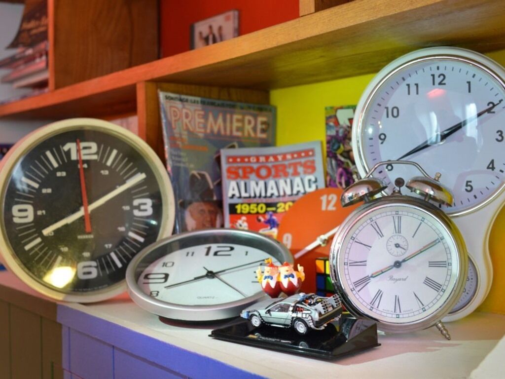 A collection of clocks on a shelf, including a sports magazine and a small toy car.
