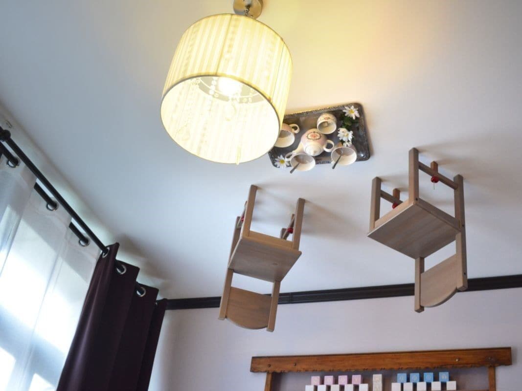 A room with a hanging wooden chair, a wall-mounted shelf with cups and saucers, and a large light fixture.