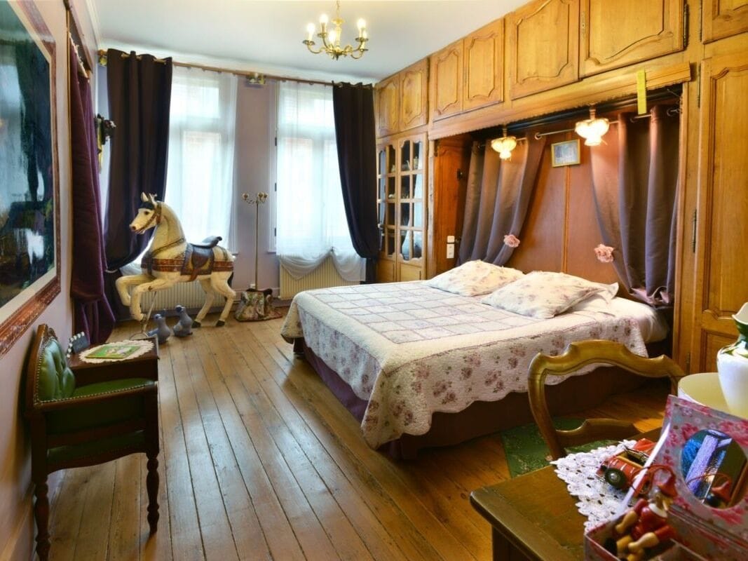 Een klassieke kamer met houten vloeren, een bed met bloemenbedekking, een schommelpaard en een houten kastje met spiegel.