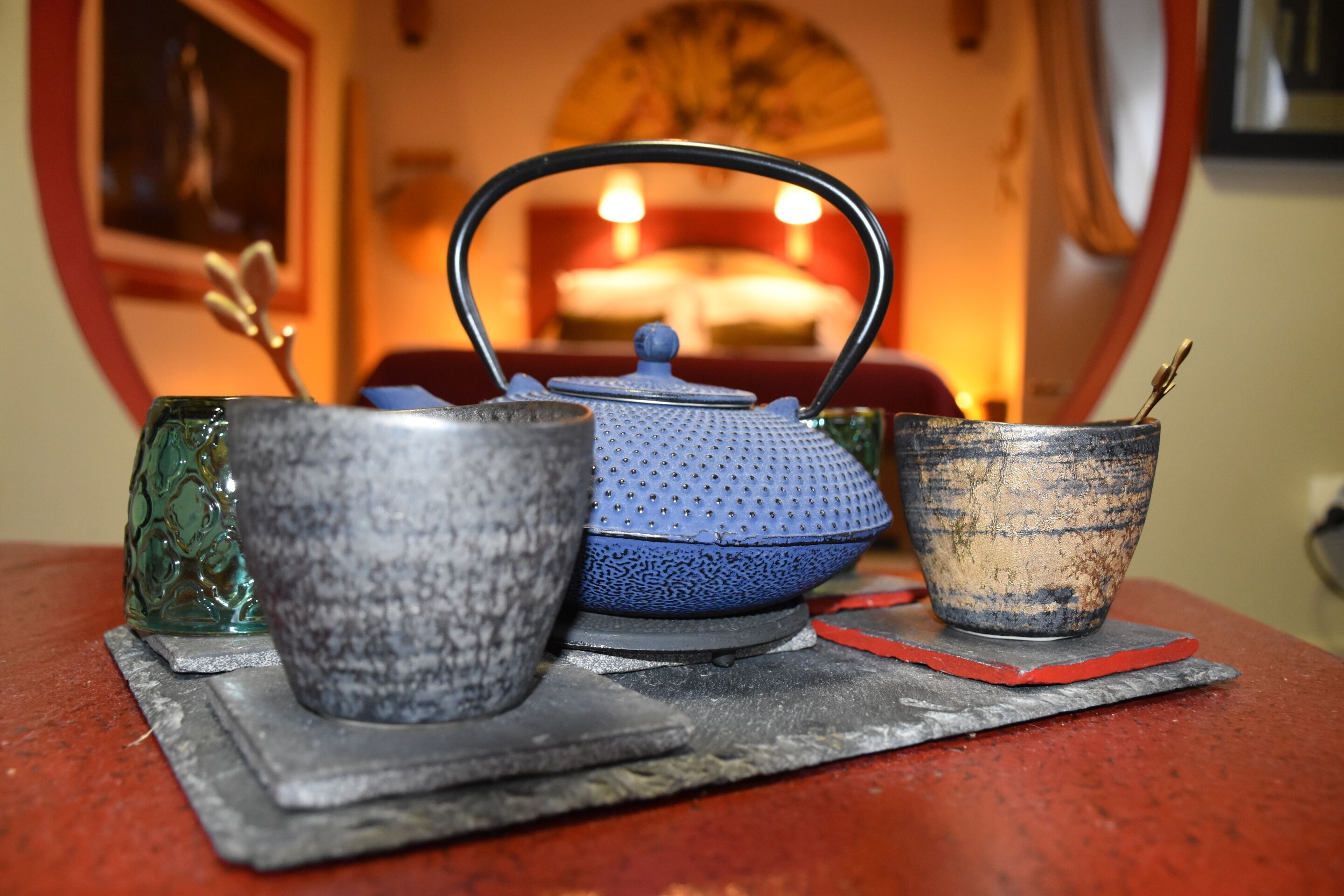 Un service à thé est posé sur une table, avec un coussin rouge et un éventail en arrière-plan.